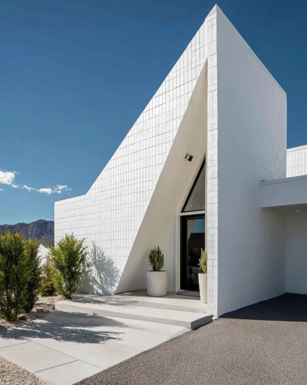 A minimalist white block A-frame building with a deeply recessed triangular entrance against a clear blue sky.