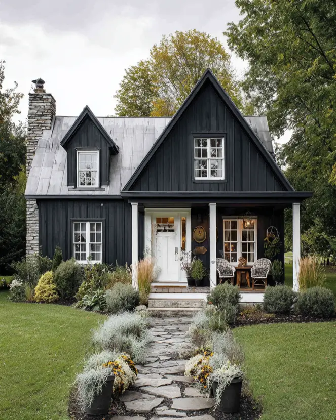 A cozy black and white farmhouse cottage with a large stone chimney and a galvanized metal roof.