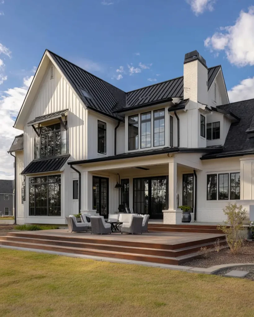 The rear of a white modern farmhouse with a multi-level wood deck and a white painted brick chimney.