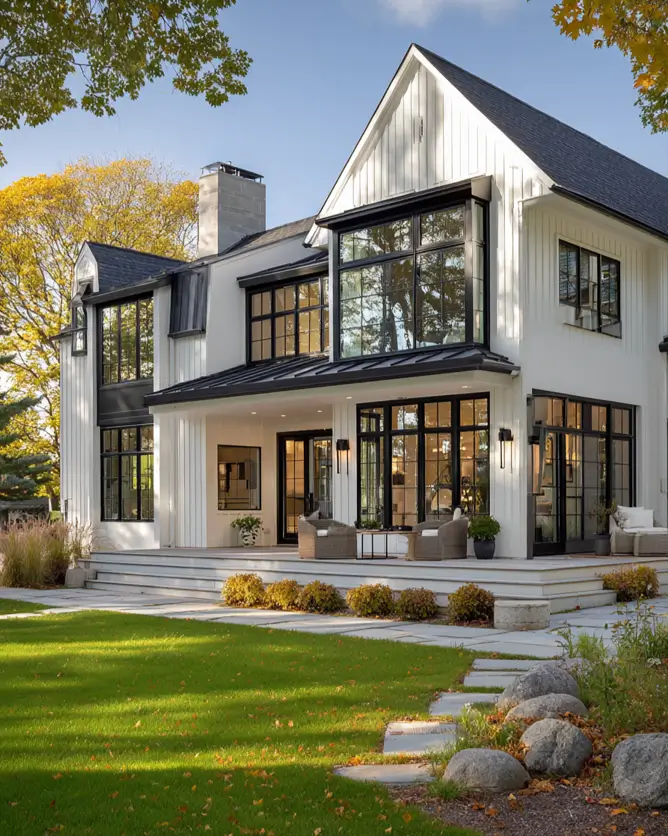 A large modern Scandinavian farmhouse with white siding and black windows, overlooking a green lawn in the late afternoon sun.