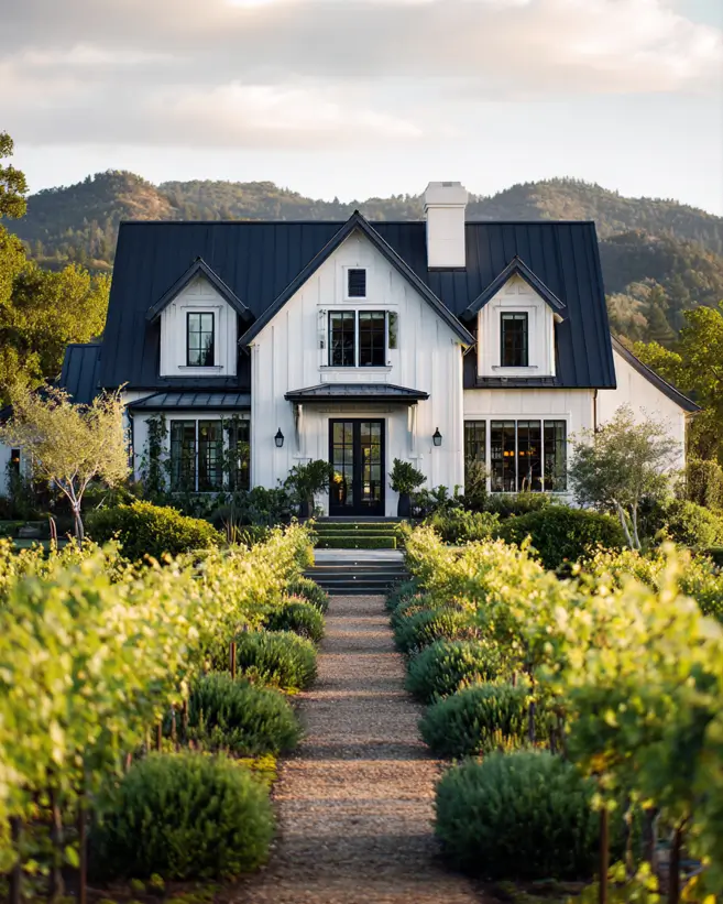 A classic white and black farmhouse exterior set in a scenic vineyard with lush green rows leading to the home.