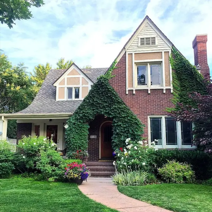 Storybook small Tudor-style house with a lush climbing ivy archway beautifully framing the front door against a timeless brick exterior.