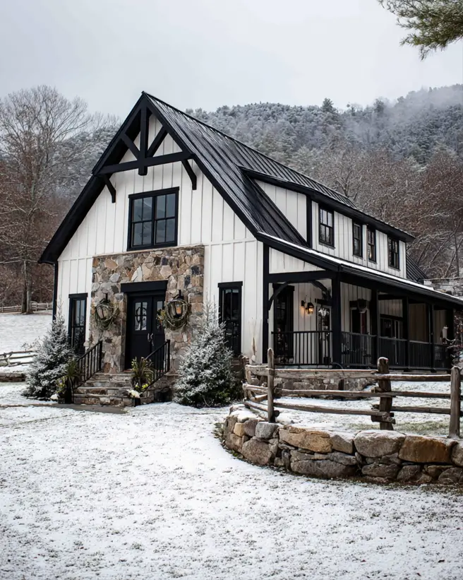 A rustic white and black farmhouse with a stone facade and timber gable, set in a snowy landscape.