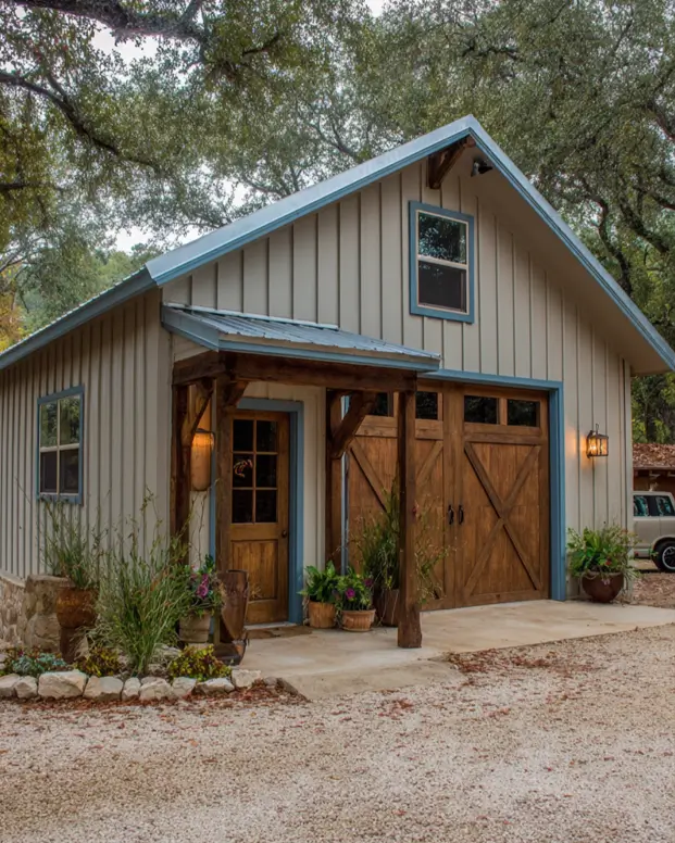 A small barndominium with beige siding, a stone foundation, blue trim, and natural wood garage and entry doors.