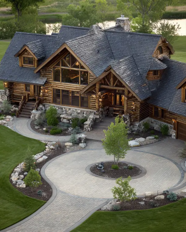 An aerial view of a large log cabin house style with a circular paved driveway and manicured lawns.