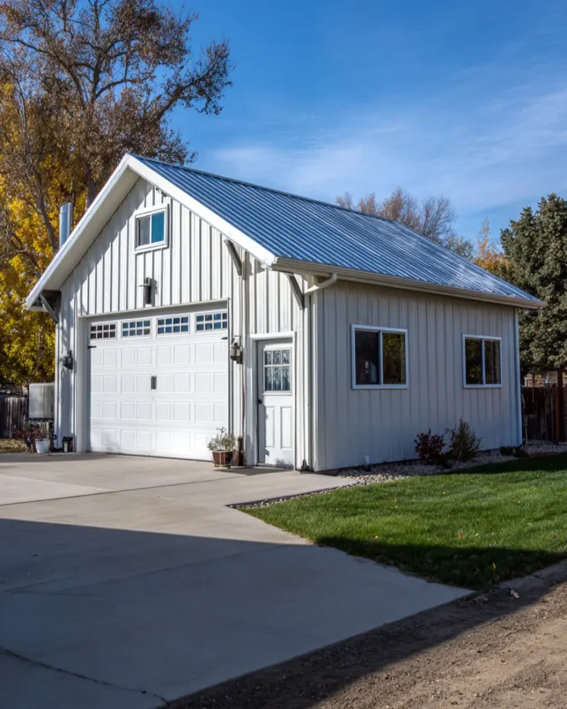 A clean-lined, small white barndominium house featuring a large two-car garage door and a metal roof under a clear blue sky.