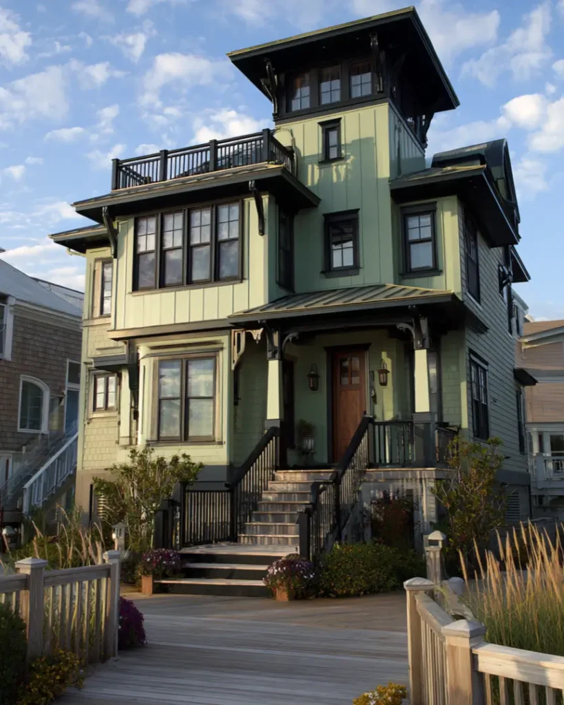 A stunning multi-level sage green beach house with extensive black trim and a rooftop lookout deck offering panoramic views.