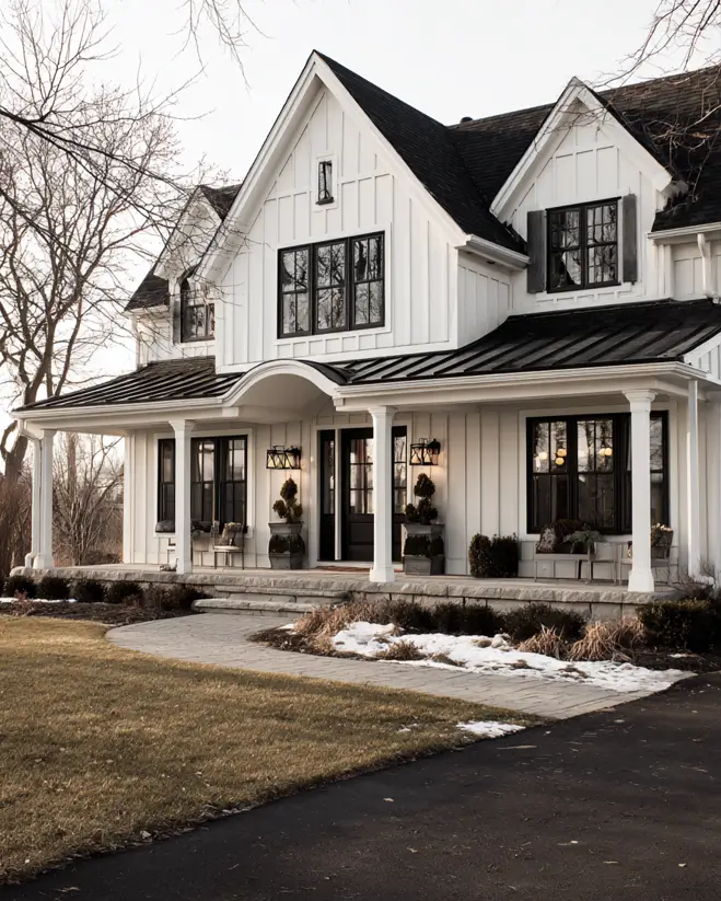 A timeless white farmhouse with black shutters and a full porch, seen in a crisp winter landscape.