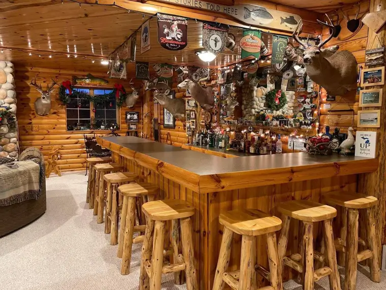 A classic bar log cabin with a large U-shaped wooden bar, rustic log stools, and walls decorated with hunting lodge decor and memorabilia.