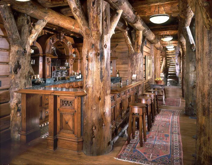 A grand and rustic bar log cabin featuring massive raw log pillars and a long, ornately carved traditional wooden bar.