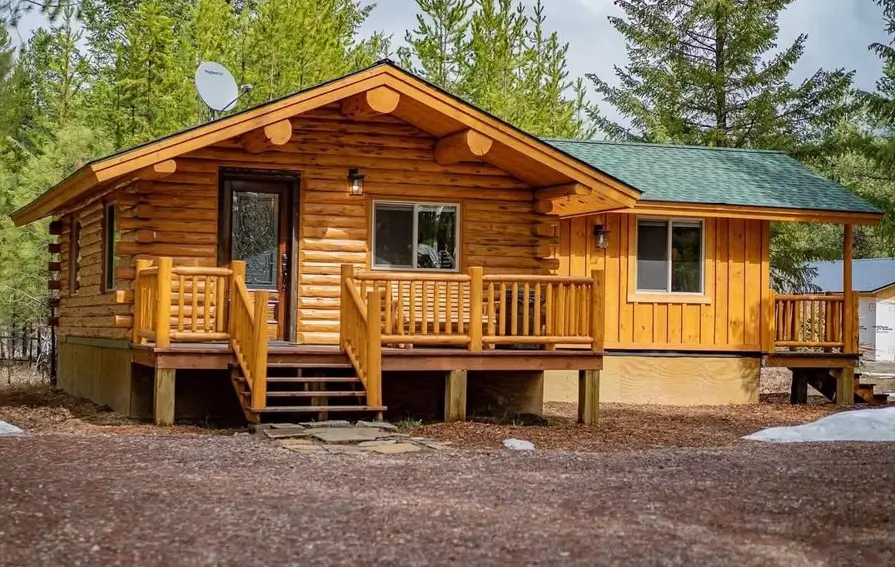 A classic log cabin house design featuring a welcoming front porch and natural wood finish, nestled among pine trees.
