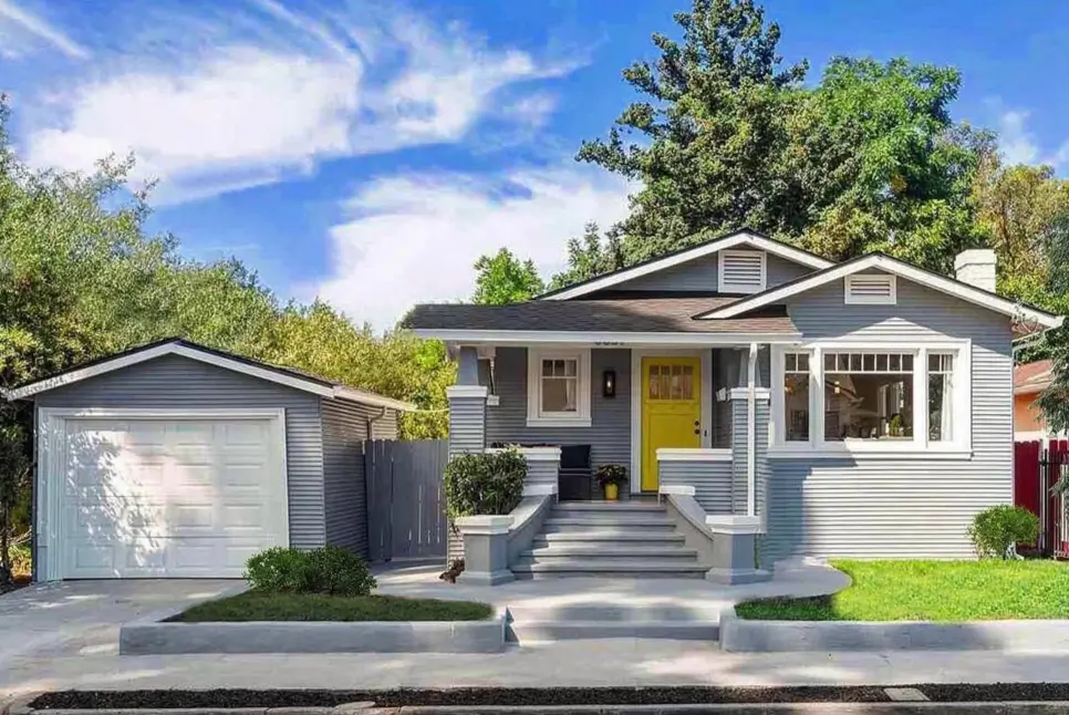 Modern craftsman bungalow with light gray siding, a bright yellow door, and a matching detached garage.