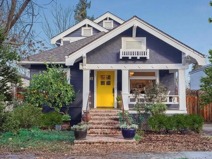 Modern craftsman bungalow with dark gray siding, thick white trim, and a vibrant, welcoming yellow front door.