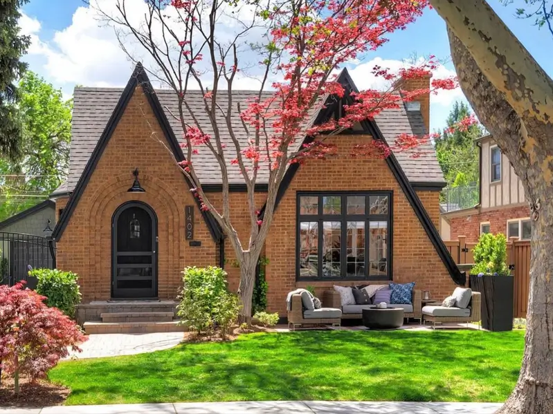 A beautiful small modern Tudor-style house with a full brick exterior, steep black gables, an arched front door, and a cozy front patio seating area.