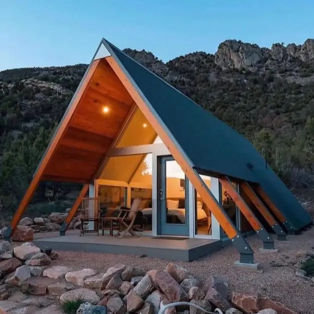 Tiny A-Frame Cabins: 31 Inspiring Ideas for Your Dream Retreat 3 A modern tiny a frame cabin with large glass windows and exposed wood beams, set in a rocky landscape at dusk.