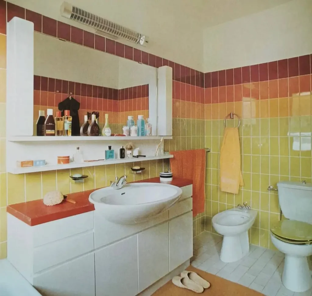 A retro 70s bathroom with gradient striped wall tile in green, orange, and red, plus a bright orange vanity top.