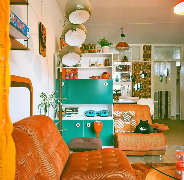 A living room embracing 70s interior design styles, featuring a burnt orange corduroy sofa, teal shelving, and globe pendant lights.