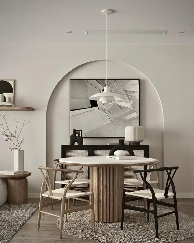 A round condo dining table with a reeded wood base and white top, surrounded by wishbone chairs in an elegant, modern dining nook.