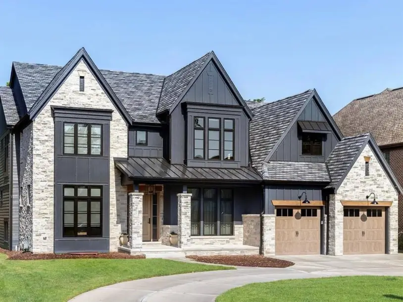 A modern black farmhouse exterior featuring light stone accents, dark siding, and natural wood garage doors.