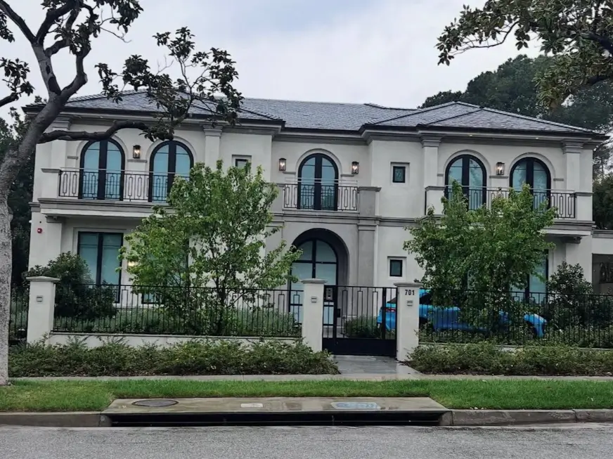 A large, modern Mediterranean home with a symmetrical facade, arched windows, and dark wrought-iron details.