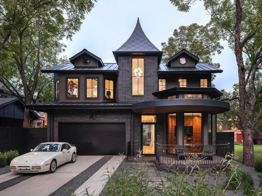 A modern Victorian style house with a dark charcoal brick exterior and a prominent turret at dusk.