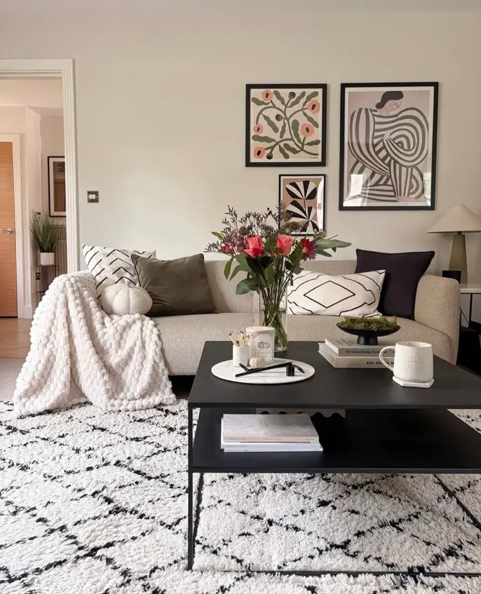 A neutral living room featuring a beige sofa layered with a textured throw, patterned pillows, and modern art on the wall.
