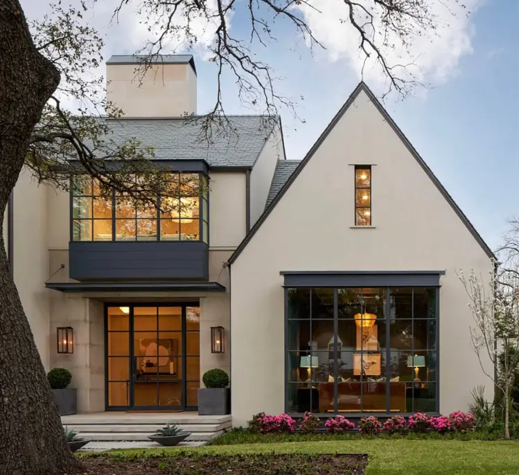 A beige and black house with large, black-framed windows, stone accents, and a prominent gable roofline.