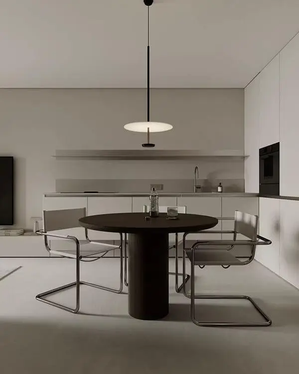 A high-contrast small condo dining room with a dark round pedestal table and light gray cantilever chairs in a minimalist kitchen.