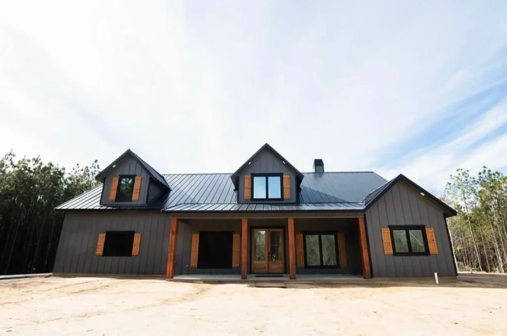 A modern black farmhouse with a metal roof, featuring rustic natural wood shutters on all the windows.
