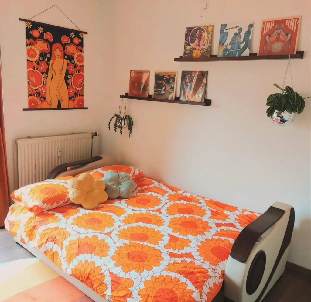 A 70s bedroom inspo look with a bright orange floral duvet, album art on the walls, and a disco ball planter.
