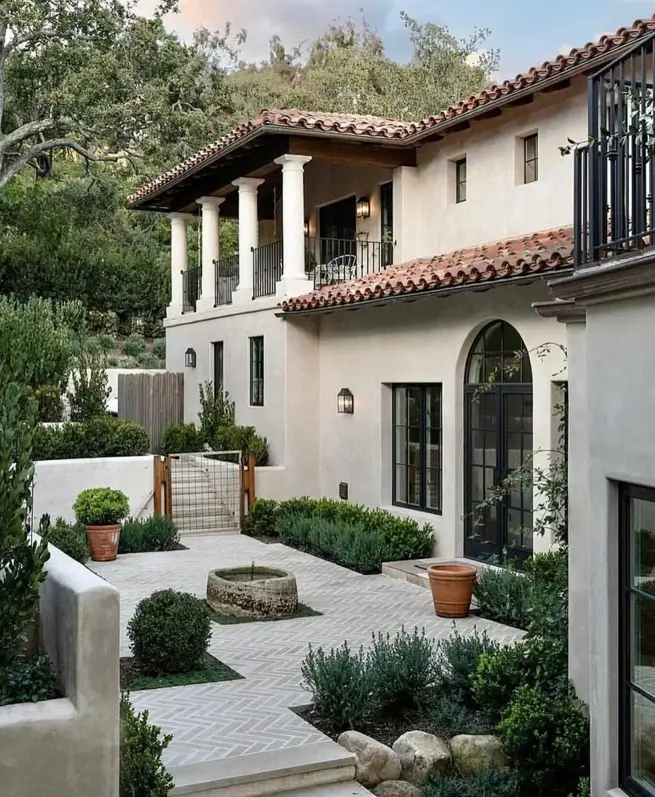 A Mediterranean villa courtyard with a herringbone brick patio, boxwood hedges, and a stone basin.