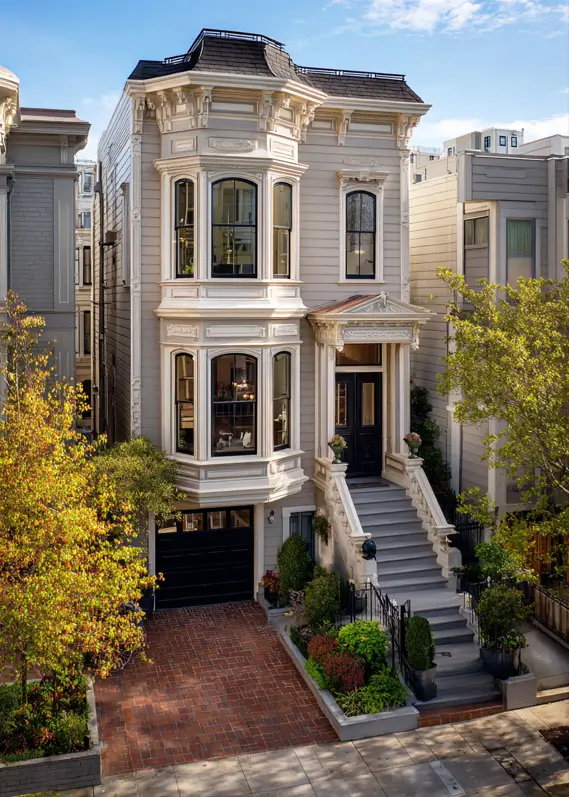 A tall modern Victorian townhouse in a warm gray color with cream trim and an integrated garage.