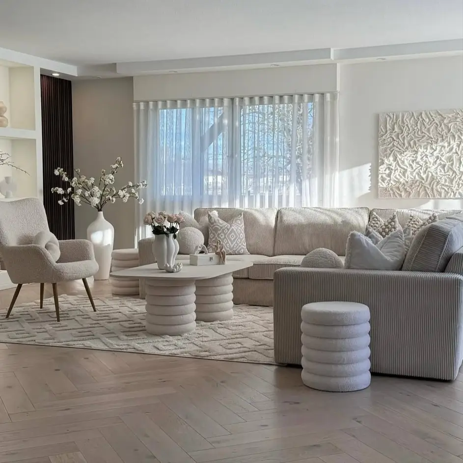 A bright, neutral living room with a corduroy sofa, bouclé chair, and textured white art on the wall.