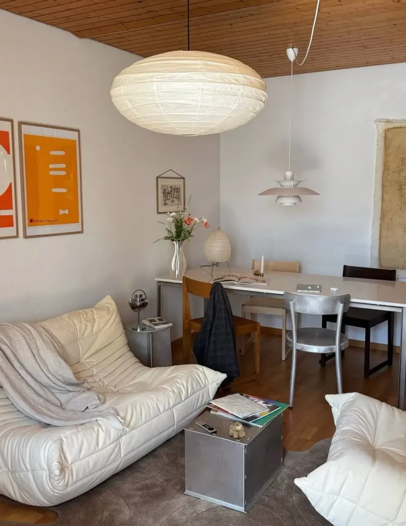 A cozy small apartment with low-slung white seating, a large paper lantern, and a dining area, showcasing a modern interior design.