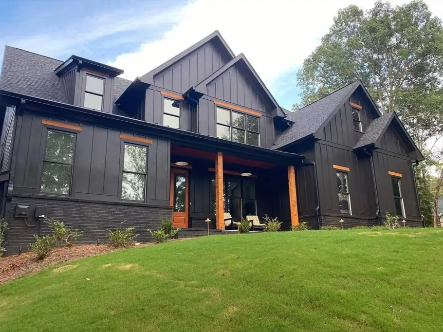 Modern black farmhouse with warm wood trim framing the windows and a dark painted brick foundation.