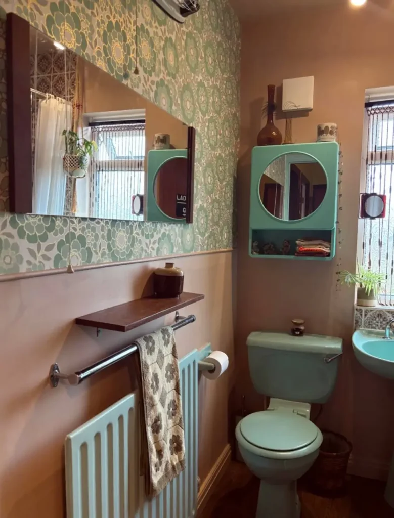 A retro 70s bathroom with green floral wallpaper, mint green fixtures, and warm brown painted walls.