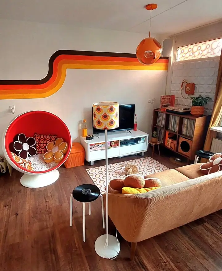 A 70s retro living room featuring a painted stripe decal, a red ball chair, and a tan sofa.