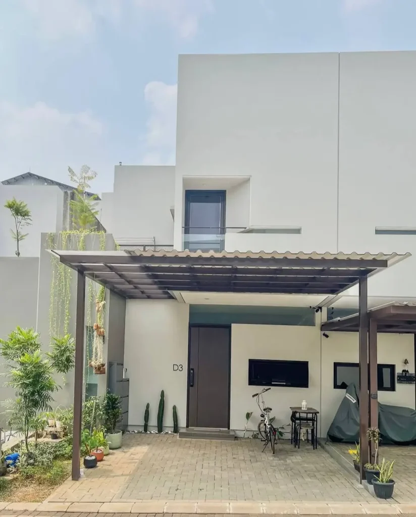 A white modern minimalist house with a simple covered carport, a paved driveway, and potted cacti.