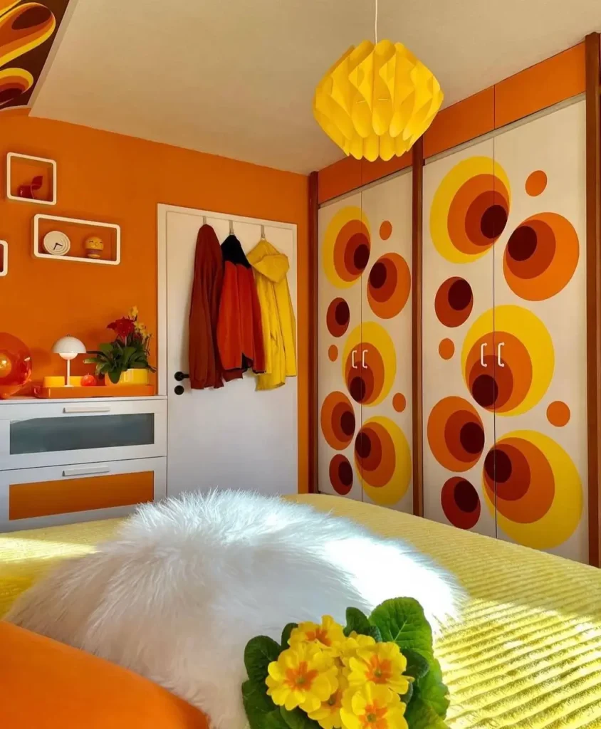 A retro 70s bedroom with bold circular graphics on the wardrobe doors and ceiling in an orange and yellow palette.