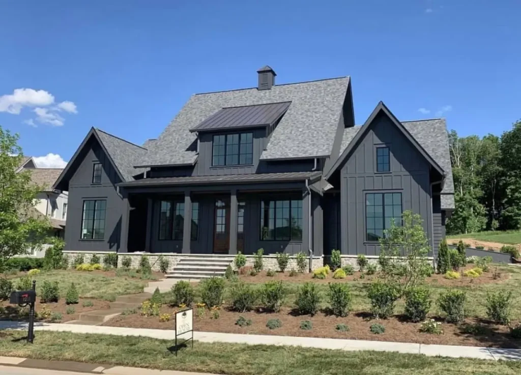 A modern black farmhouse exterior with layered gables, a metal roof accent, and a large covered front porch.