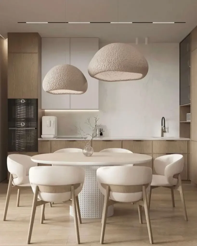 A round dining table with light upholstered chairs set under two large, textured dome pendant lights in a modern condo kitchen.