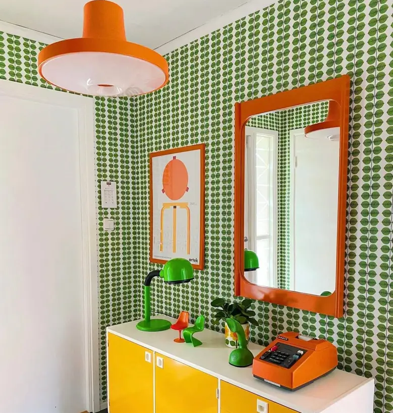 An entryway with 70s interior design, featuring green graphic wallpaper, an orange mirror, and a yellow cabinet.