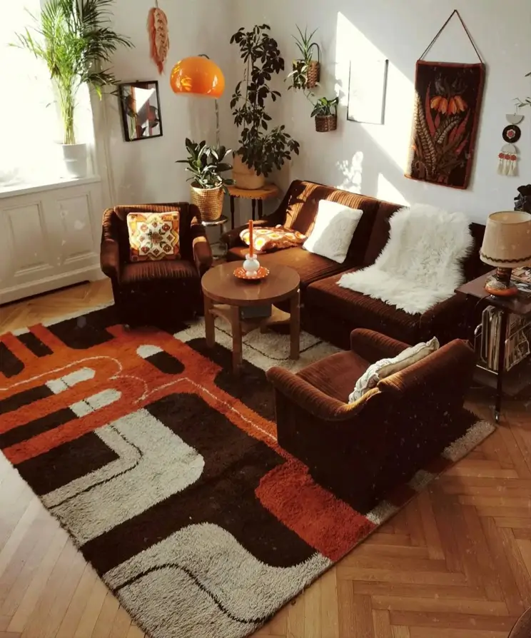 A 70s living room with a brown velour sofa, a large graphic rug, and numerous plants.