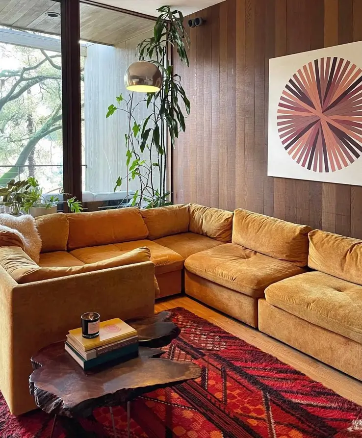 A 70s living room featuring wood-paneled walls, a gold modular sofa, and a red patterned rug.