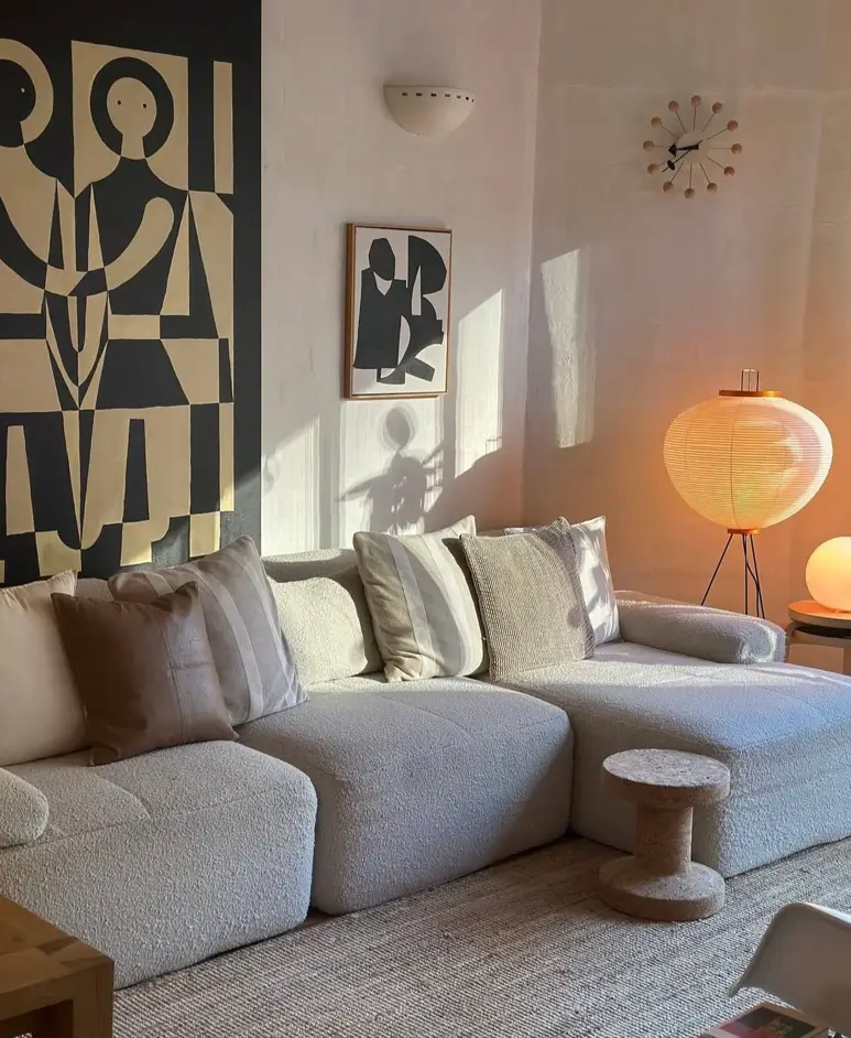 A cozy small apartment corner featuring a textured sofa, curated abstract wall art, and a paper lantern lamp casting warm light.