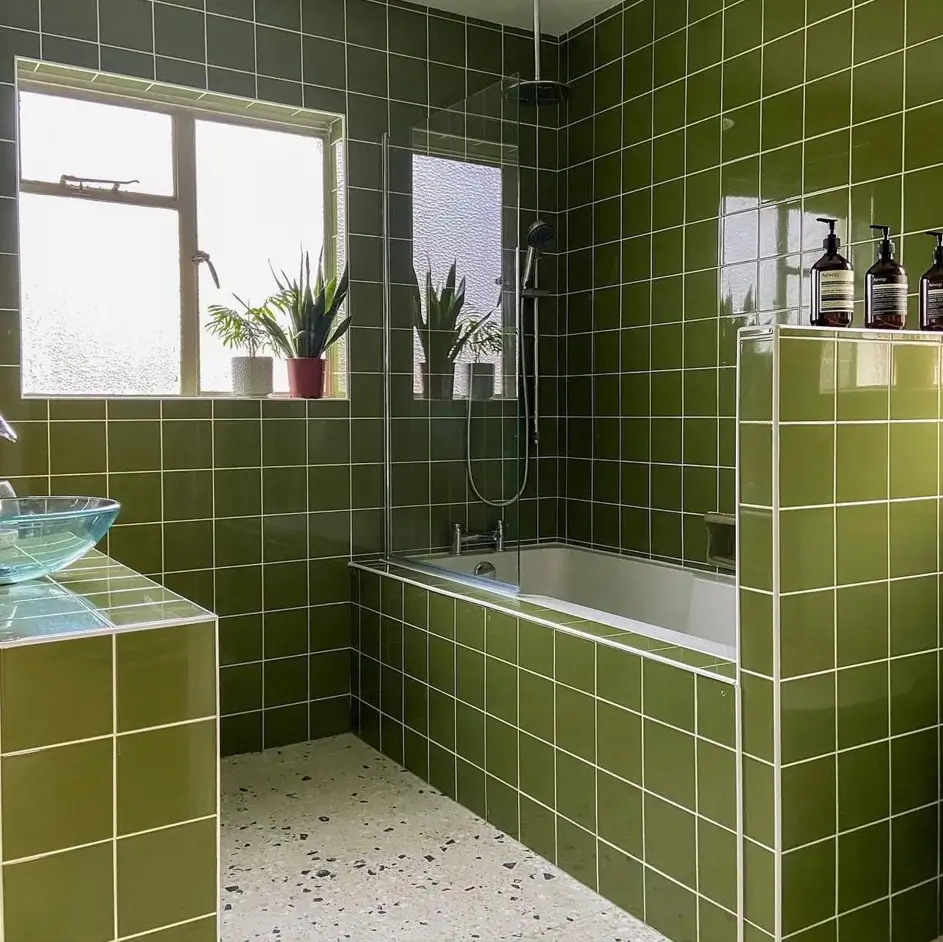 A modern 70s bathroom featuring floor-to-ceiling avocado green tile and a light terrazzo floor.