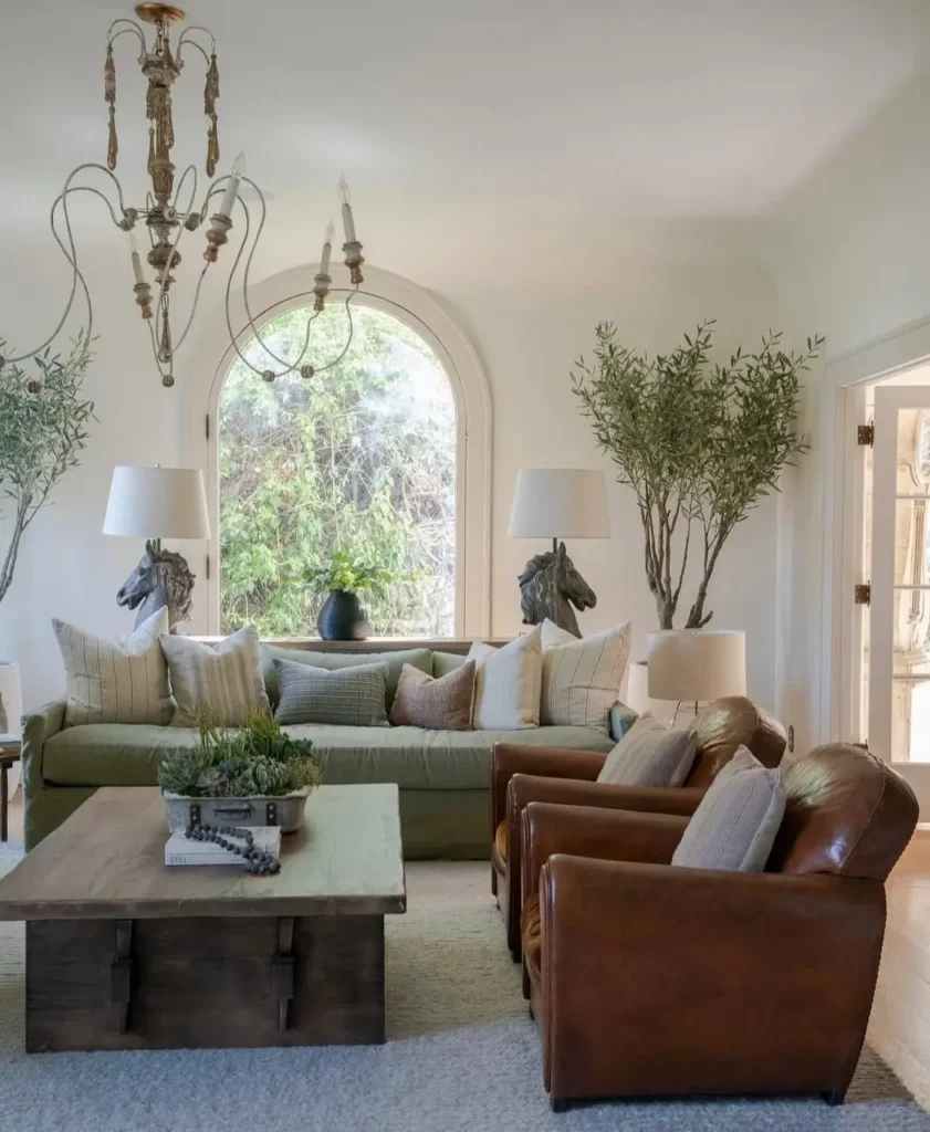 A living room with a sage green sofa, two brown leather armchairs, and a large arched window in a neutral setting.