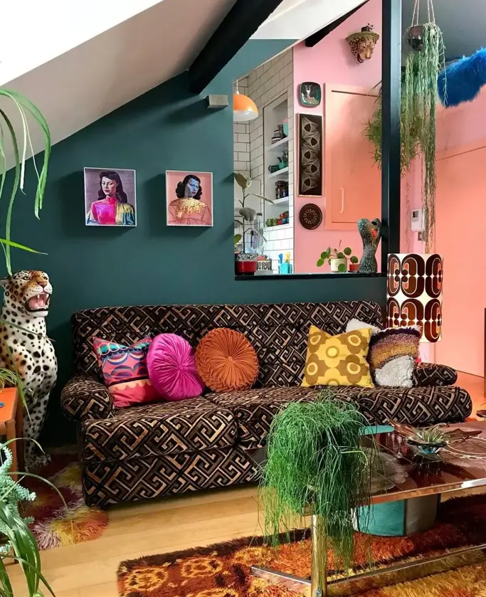 An eclectic living room with 70s interior decor, featuring a geometric patterned sofa, a teal wall, and colorful pillows.