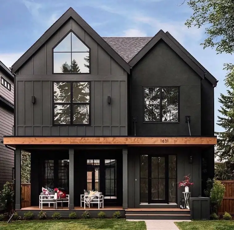 A modern black farmhouse with a large triangular gabled window and a full-width front porch with a wood ceiling.