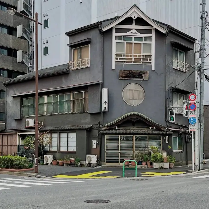 A traditional Japanese style house on a corner with grey stucco and a round window.